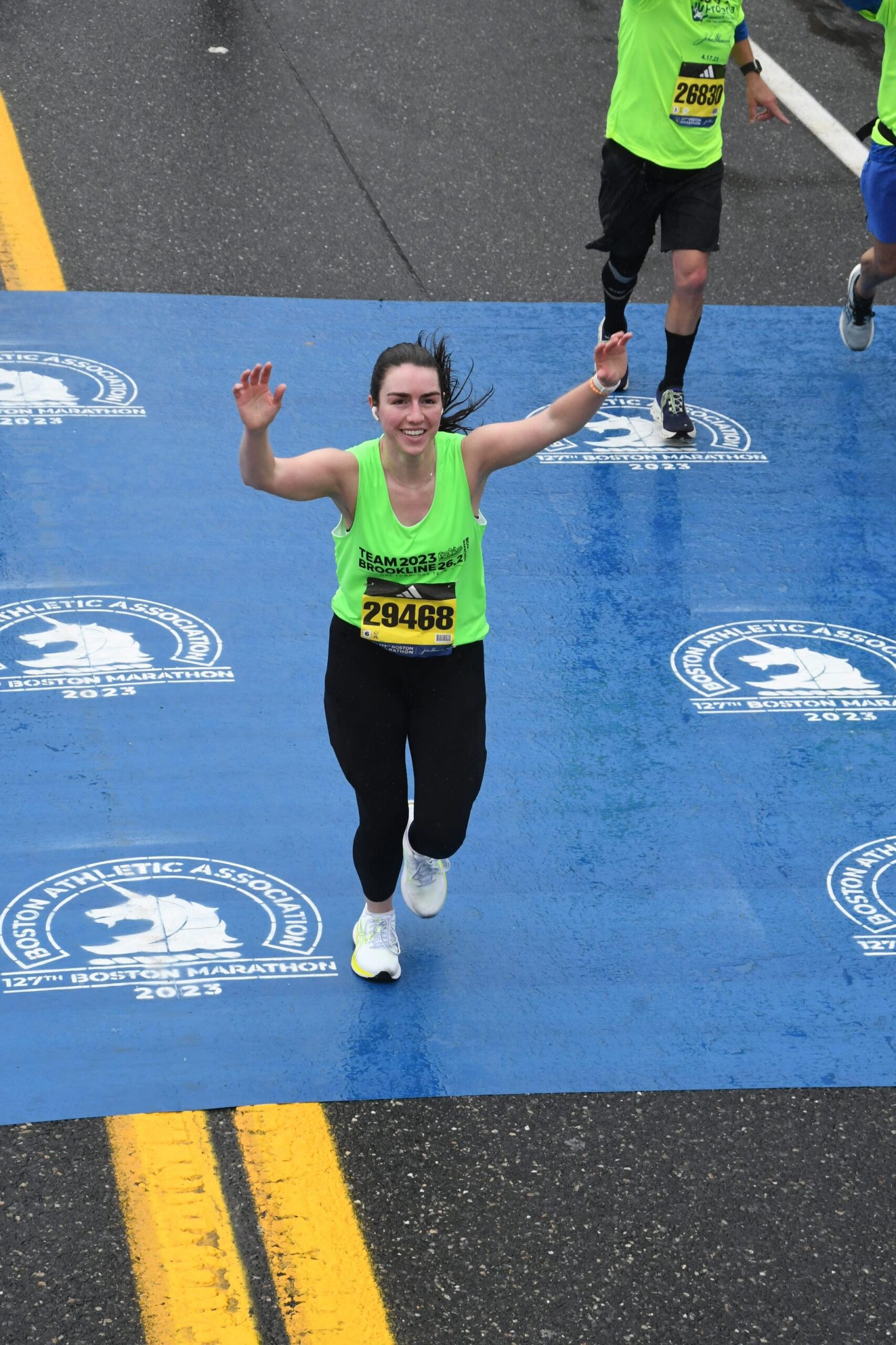 Erin Murdock waving as she runs across the Boston Marathon finish line