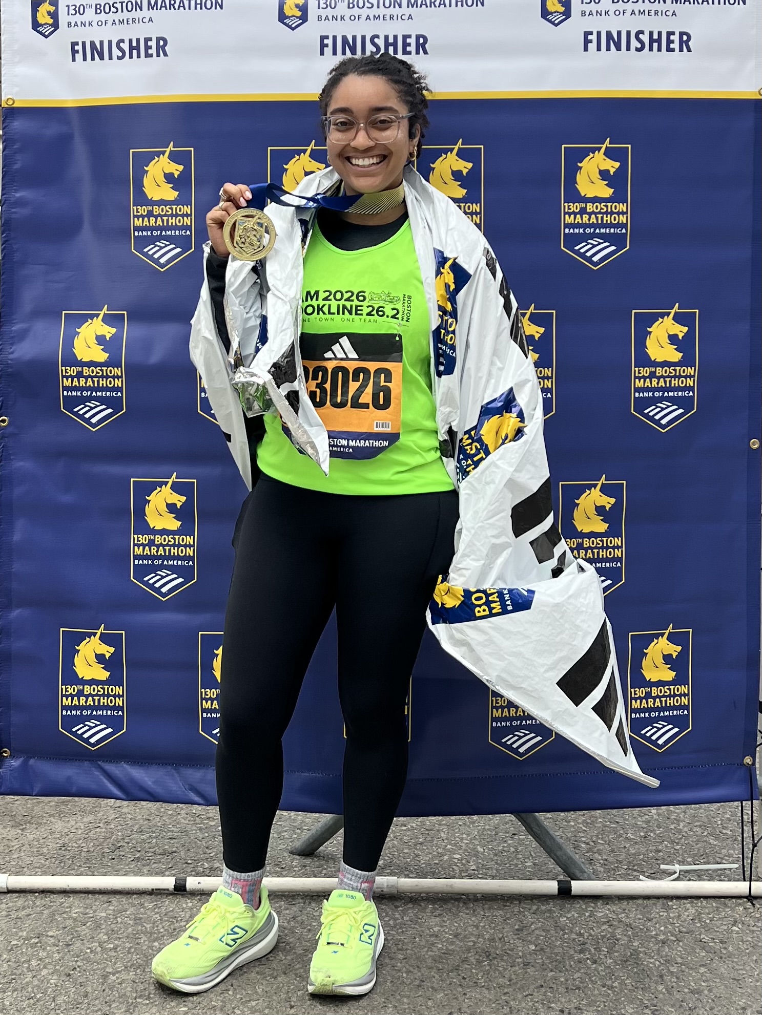 A Team Brookline runner holding up her Boston Marathon finisher medal